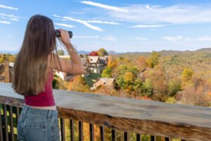 Guest enjoying scenic Smoky Mountain views from the private balcony overlooking colorful fall foliage and nearby mountain cabins.